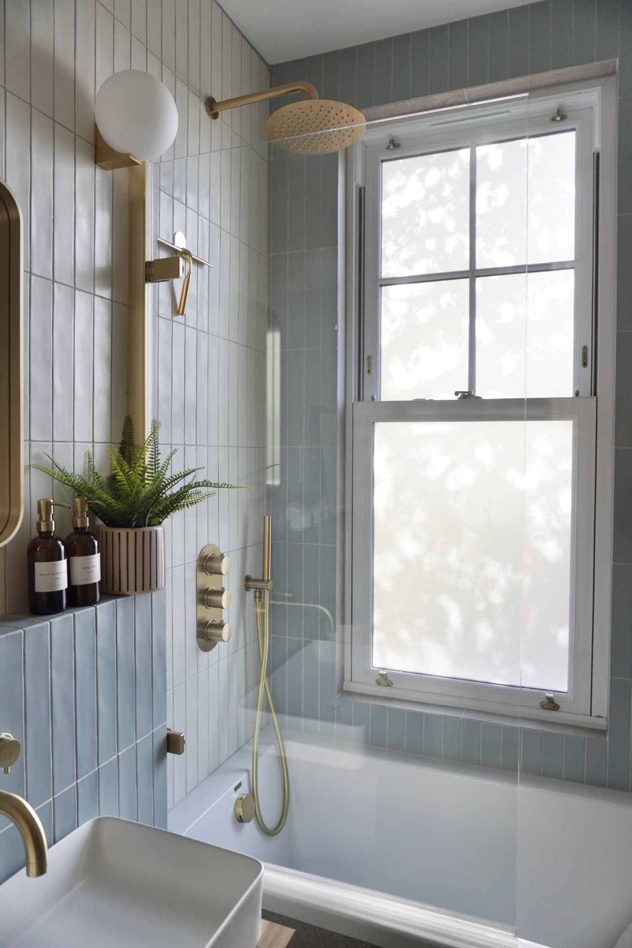 Bathroom with white and sage tiles, brass fittings and a sash window