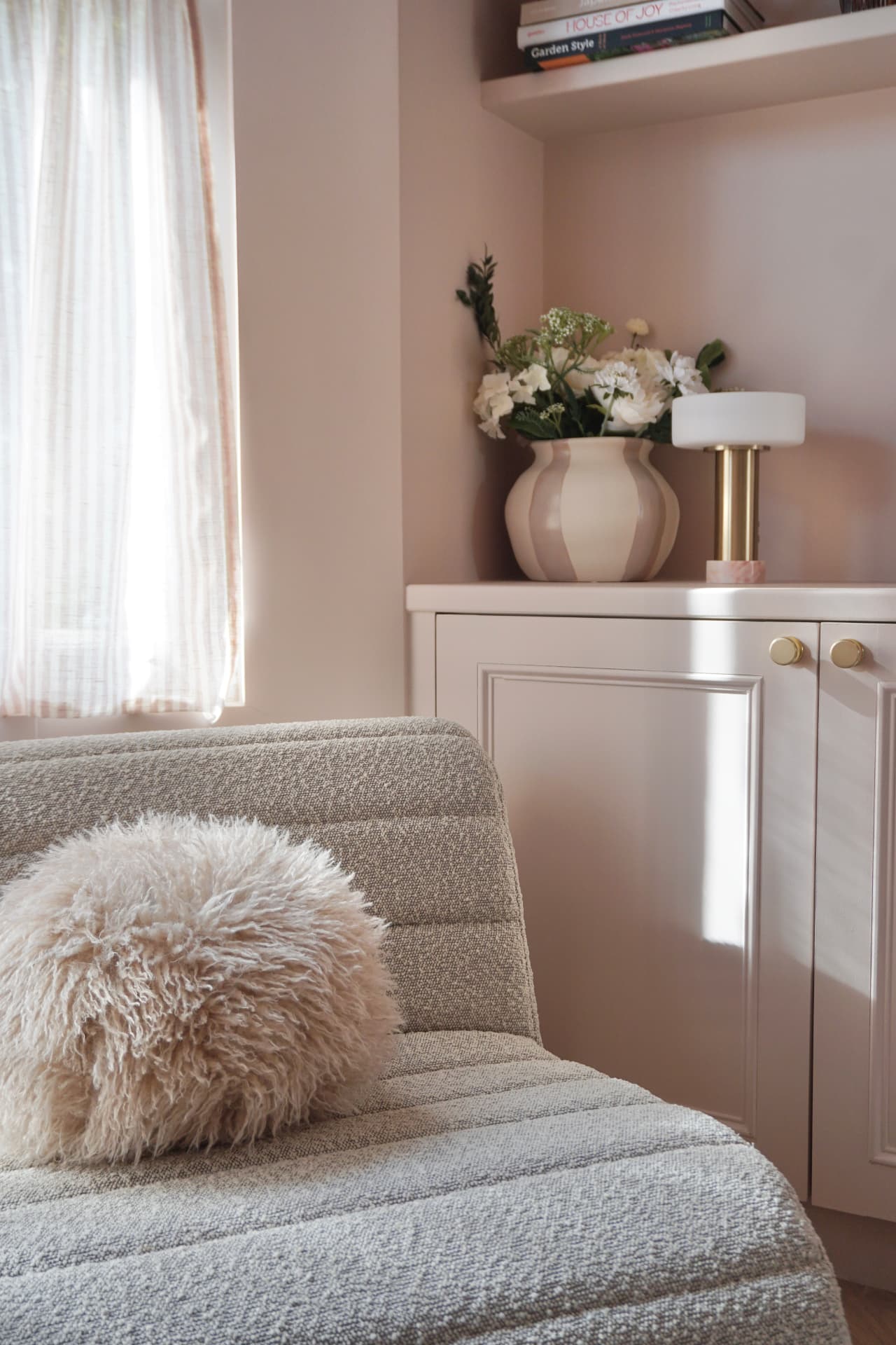 Boucle chair with a sheepskin cushion beside a pink cabinet styled with flowers