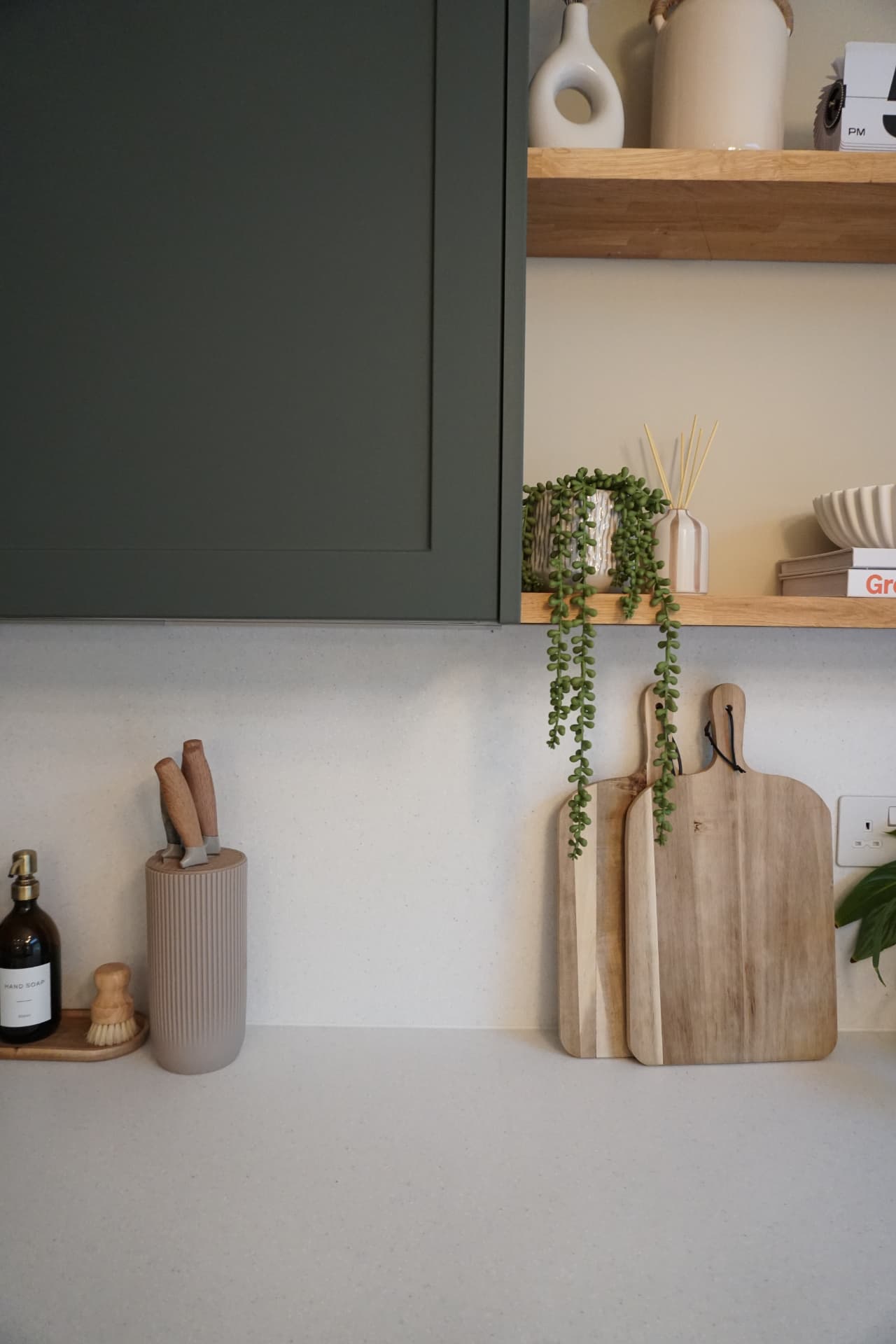 Open-plan kitchen and living space with dark green cabinetry and oak shelves