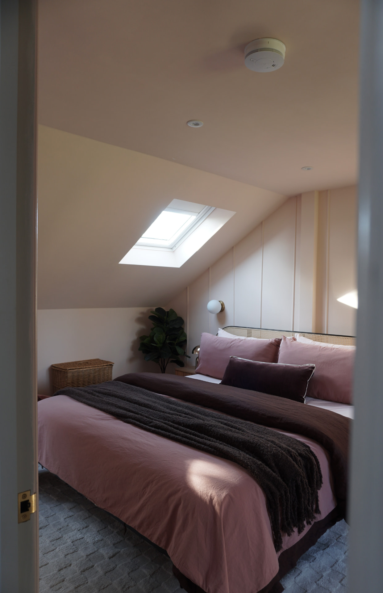 Master bedroom under the skylight with pink bedding and a chocolate throw