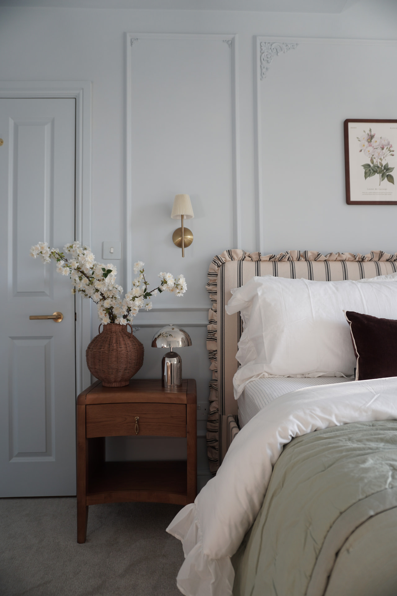 Blue bedroom with blossom in a wicker vase and a striped headboard