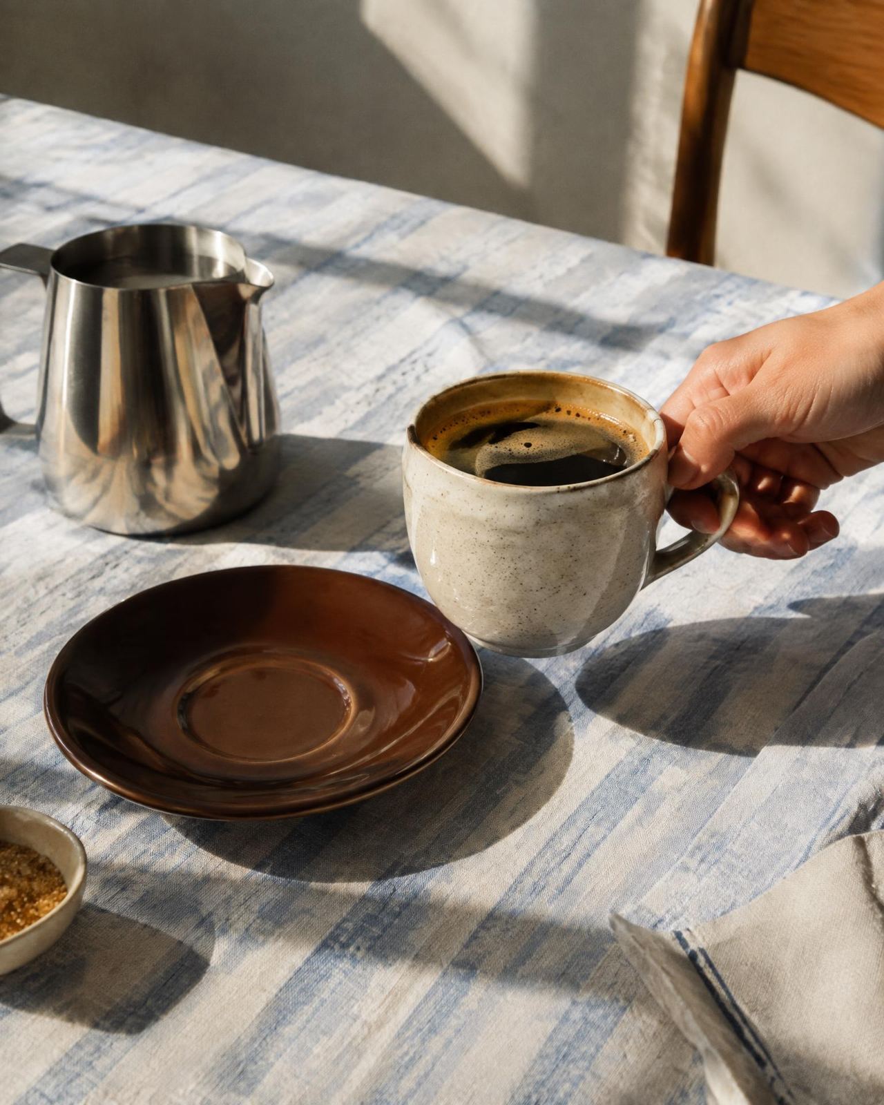 Hand holding a ceramic coffee cup on striped linen