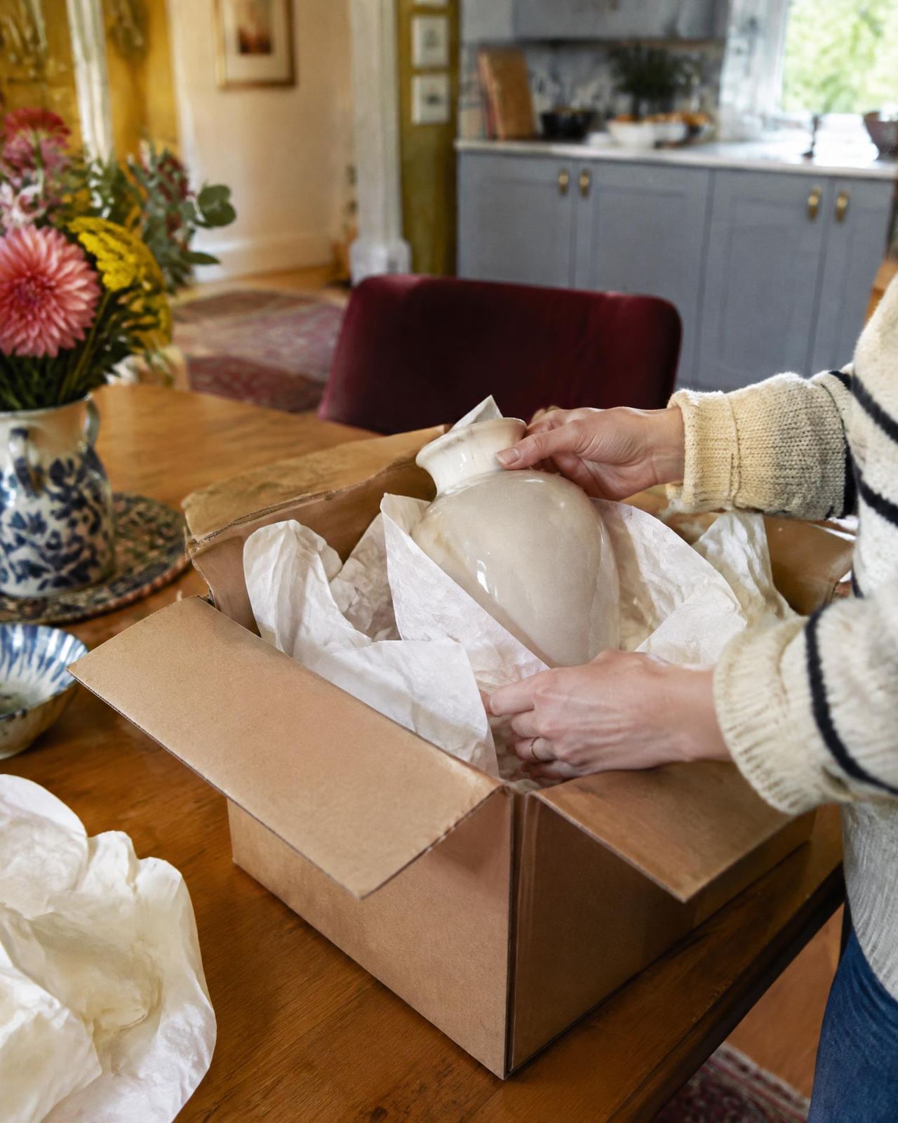 Unboxing a cream ceramic vase on a dining table